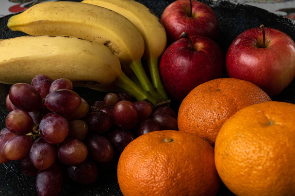 Üç üzüm, mandalina, muz ve elma, siyah bir tencerede. - Fotoğraf, Görsel