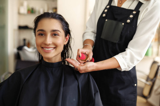 Парикмахер наносит мусс на волосы женщин, вид спереди, парикмахерскую. Стилист и клиент в парикмахерской. Бизнес красоты, профессиональное обслуживание - Фото, изображение