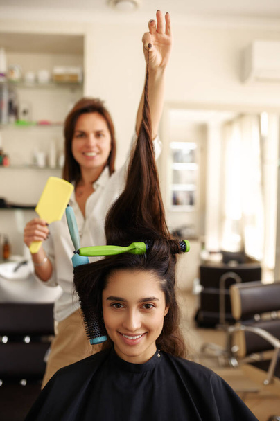 Жіночий перукар завиває жіноче волосся, перукарня. Стиліст і клієнт у шерстяному салоні. Краса бізнесу, професійне обслуговування
 - Фото, зображення