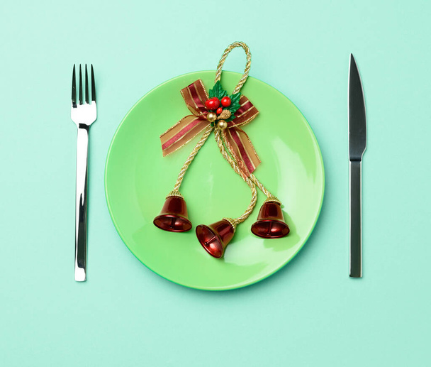 vihreä pyöreä punainen keraaminen levy, veitsi ja haarukka vihreällä taustalla, juhlapöydän kattaminen jouluksi ja uusi vuosi, ylhäältä - Valokuva, kuva