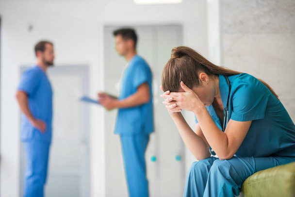 Young female doctor feeling unhappy while her colleagues talking - Photo, Image