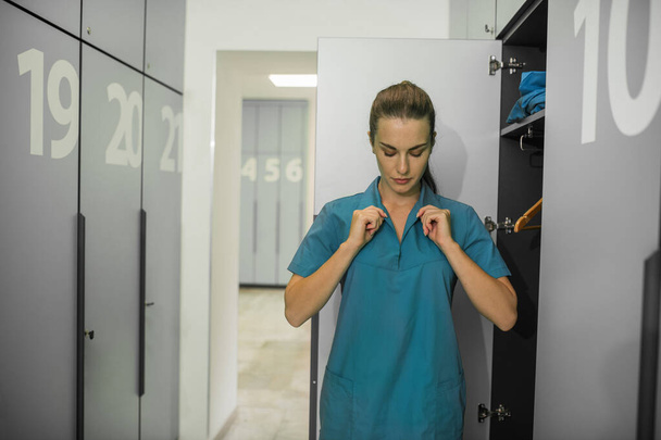 Long-haired young female doctor changing clothes in the locker room - Photo, Image