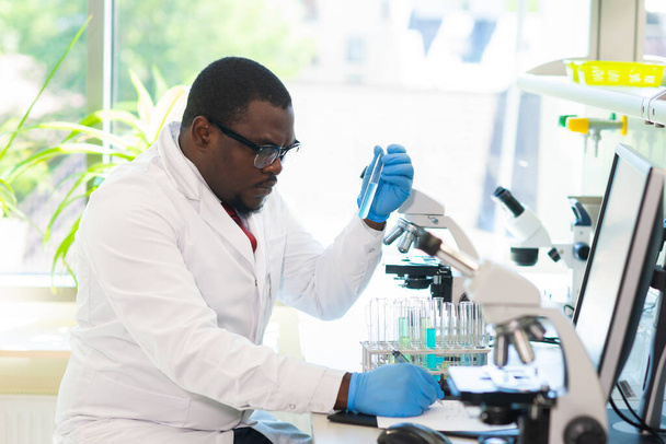 African-american Medical doctor working in research lab. Science assistant making pharmaceutical experiments. Laboratory tools: microscope, test tubes, equipment. Chemistry, medicine, biochemistry - Valokuva, kuva