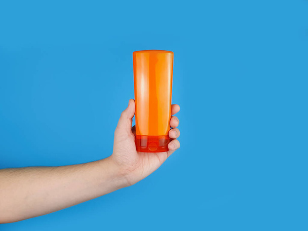 Mockup de xampu laranja sem marca e garrafa condicionador para branding e rótulo e mão masculina sobre fundo azul. Minimalismo. - Foto, Imagem