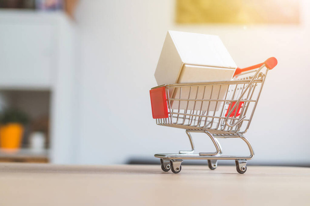 Online-Shopping and parcel service concept: Miniature shopping cart and white box - Fotoğraf, Görsel