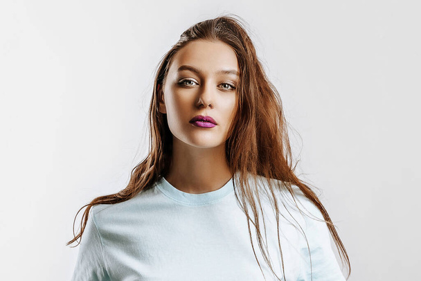 Beautiful young brunette girl with green eyes with long hair with fashion makeup with purple lips on an isolated gray background. The woman seriously looking at the camera. Kind cute model - Φωτογραφία, εικόνα