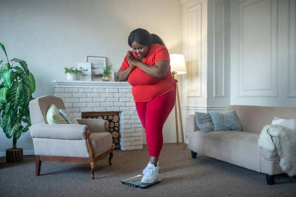 Plus rozmiar Afroamerykanka amerykańska kobieta sprawdza swoją wagę i wygląda na zszokowaną - Zdjęcie, obraz