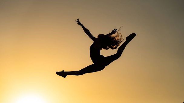 Female flexible dancer jumping during sunset on the orange sky background. Concept of freedom and happiness  - Foto, imagen