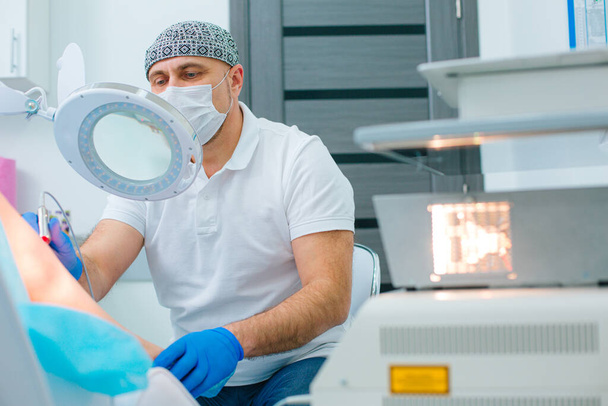 Serious dermatologist in medical mask performing laser spider veins removal in modern clinic - Fotó, kép