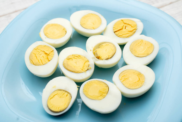 Boiled eggs cut into two halves on a blue plate on a white wooden background. - Фото, зображення