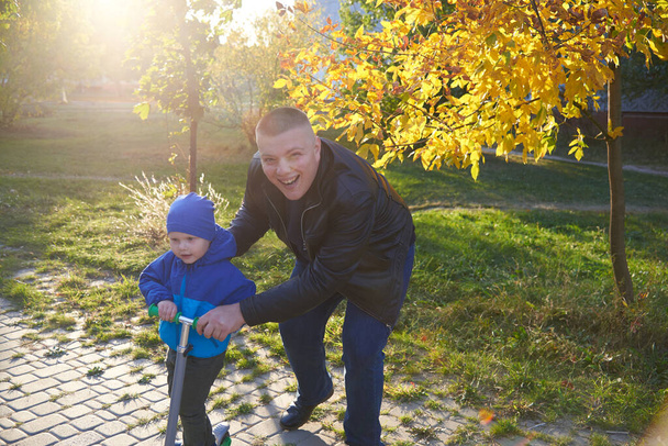 父は秋に公園でスクーターに乗るために彼の2歳の息子を教えています. - 写真・画像