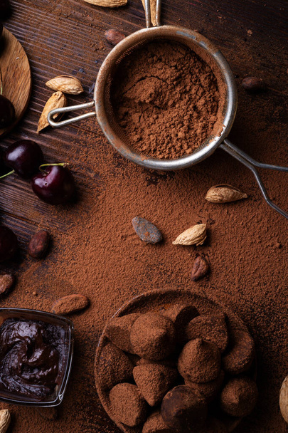art background with healthy delicious dark truffles, chocolate  and  ingridients:  natural cocoa beans,  powder, chocolate, almonds  nuts and  ripe cherry. healthy sweets concept. flat lay - Foto, imagen