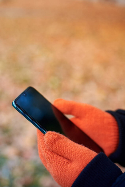 Nő kezét narancssárga kesztyű tart egy okostelefon őszi alapon. - Fotó, kép