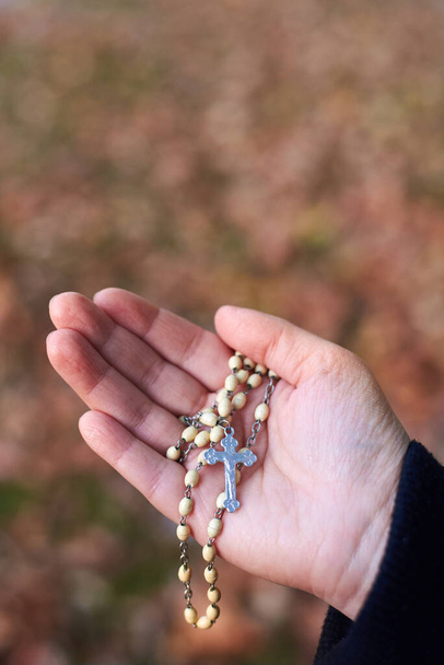 Women's hands holding rosary at the autumn background, close-up. - Photo, Image