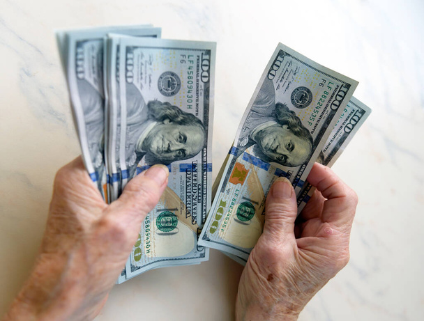 100 dolarlık banknotlar halinde para tutan yaşlı bir kadının yakın çekimi. - Fotoğraf, Görsel