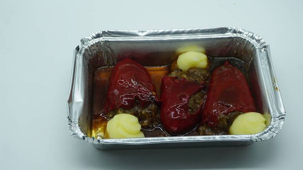 Paprika gefüllt mit geschmortem Ochsenschwanz, in einem Aluminiumbehälter zum Mitnehmen in einem Restaurant. Ich nehme Essen zum Mitnehmen. Restaurants zum Mitnehmen wegen der Covid-19-Pandemie. - Foto, Bild