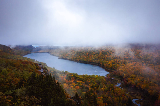 Bella foto aerea di viaggio del lago delle nuvole Si affacciano come la nebbia si solleva dagli alberi sottostanti in una mattina nuvolosa con fogliame colorato autunno che copre le colline e la valle sottostante. - Foto, immagini