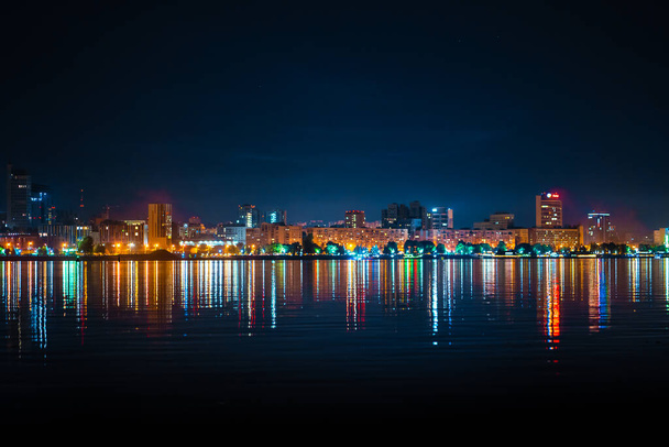 ночной пейзаж городской набережной со множеством цветных огней, отраженных в воде. - Фото, изображение
