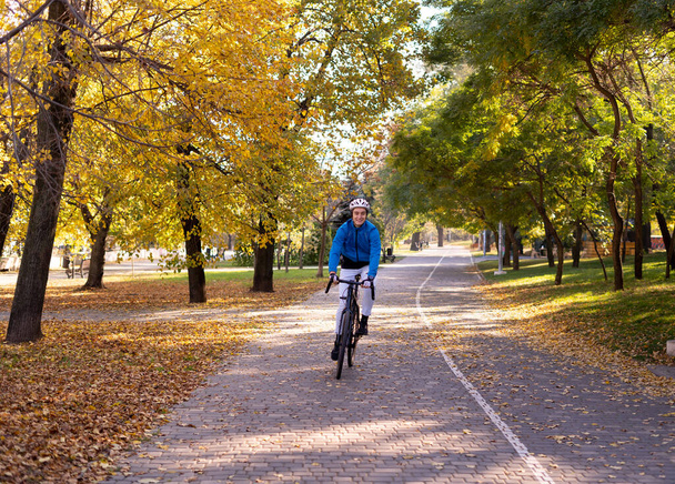 Ο νεαρός καβαλάει ποδήλατο στο πάρκο. Αθλητής με κράνος και κοστούμι. - Φωτογραφία, εικόνα