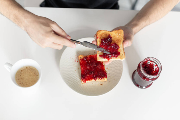 Top view spreads cherry jam on toast. - Zdjęcie, obraz