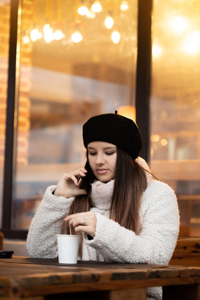 Young girl drinking coffee while she is talking on her phone. Girl Drinking coffee in a cozy restaurant. - Фото, зображення