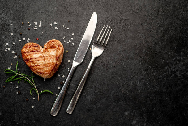 grillezett csirkehús szív alakú fűszerekkel és fűszernövényekkel sötét alapon  - Fotó, kép