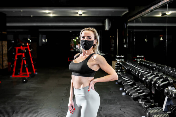 joven mujer usando máscara posando después de ejercicios de fitness en el gimnasio - Foto, Imagen