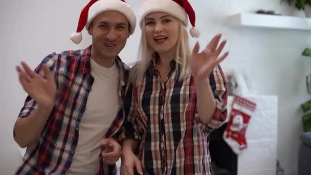 Egy pár együtt tölt egy kis időt otthon. Vonzó fiatal nők és jóképű férfi egyaránt viselnek Mikulás sapkát, hogy megünnepeljék a karácsonyt. fogalom Család, szerelem, boldogság, ünnepek és ünneplés. - Felvétel, videó
