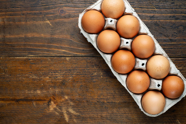 Chicken eggs in a tray on a wooden table. Breakfast products concept. Top view. Space for text. - 写真・画像
