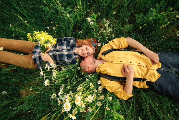 happy young couple man and redhead woman lying on bright green grass on summer day, top view. Love story - Foto, imagen
