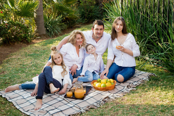 Iso onnellinen perhe lepää eväsretkellä aurinkoisena kesäpäivänä. Isä, äiti, kaksi tytärtä ja yksi poika yhdessä. Perhe valkoisissa paidoissa ja farkuissa juo ja syö. Kansainvälinen perhepäivä - Valokuva, kuva