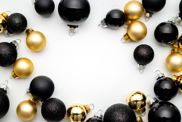 Happy winter holiday. Black baubles, golden balls in Christmas decoration on white background for greeting card. Flat lay, top view, copy space. - Photo, Image