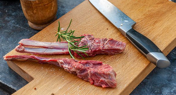 Delicious lamb chops with rosemary and spices and big knife on wooden cutting board  - Фото, зображення