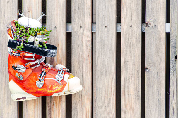 Bottes de ski anciennes orange comme un pot de fleurs suspendu sur une clôture légère en bois, fond avec espace de copie - Photo, image