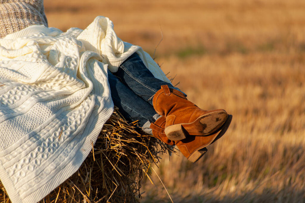 Ženské nohy v semišových kovbojských botách zabalené v bílé přikrývce na podzimním poli na seně, slunečný den  - Fotografie, Obrázek