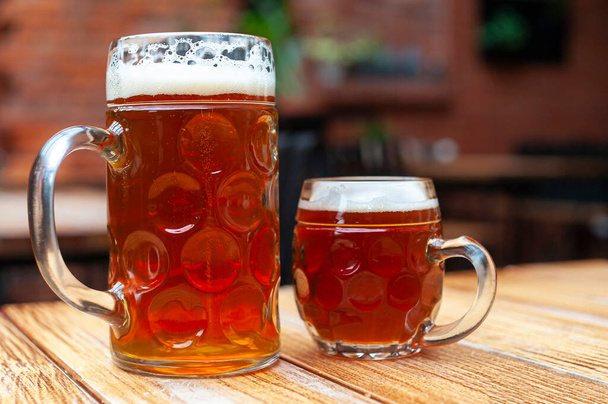 2 canecas de cerveja com cerveja âmbar - grande e pequeno, na mesa de madeira no pub  - Foto, Imagem