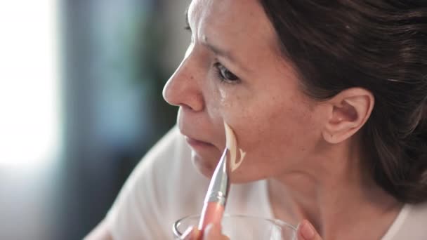 Lähikuva houkutteleva sekoitettu rotu nainen hänen 40s soveltamalla nestemäinen kotitekoinen naamio kasvot tuuletin brash kattaa kaikki vyöhykkeet ravitseva nuorentava vaikutus - Materiaali, video