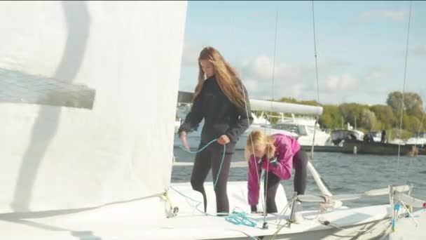 Twee schattige meisjes staan op het achterschip van een wit sportjacht en trekken aan de touwen om het zeil te controleren - Video