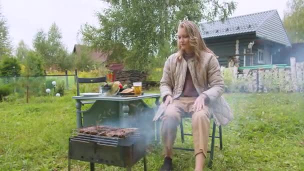 Donna triste solitario è annoiato nel cortile di una casa di campagna, lei fa un barbecue e beve birra nel bel tempo - Filmati, video