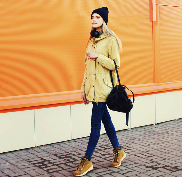 Elegante mujer rubia joven modelo caminando en la ciudad sobre un fondo naranja - Foto, imagen