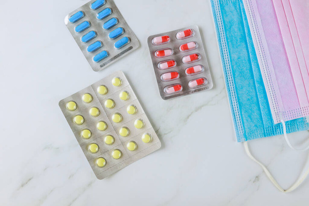 Куча пузырьков с различными таблетками и капсулами на медицинской защитной хирургической маске - Фото, изображение