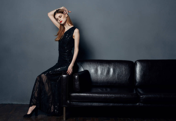 Вид сбоку женщины, сидящей на диване в черном платье на заднем плане внутри - Фото, изображение