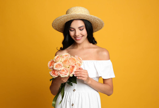 Portrait of smiling woman with beautiful bouquet on orange background - Фото, изображение
