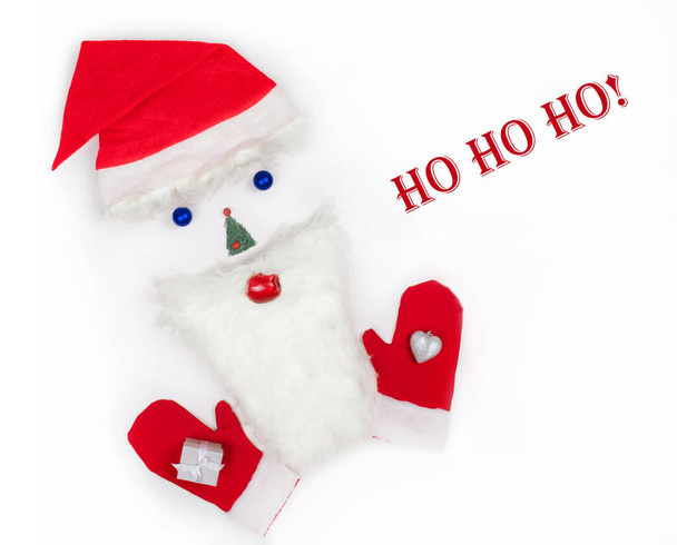クリスマス・ホー・ホー・グリーティングカード。白い背景にクリスマスのおもちゃ、モミの木、ひげとサンタのミトンで作られたサンタクロースの顔。クリスマスのシンボル。創造的だ。フラットレイアウト、コピースペース、トップビュー. - 写真・画像