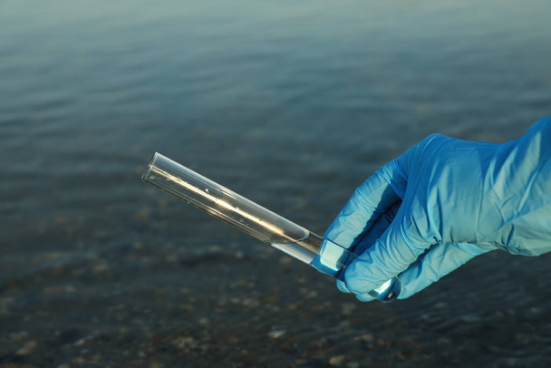 Scientist with test tube taking sample from river for analysis, closeup - 写真・画像