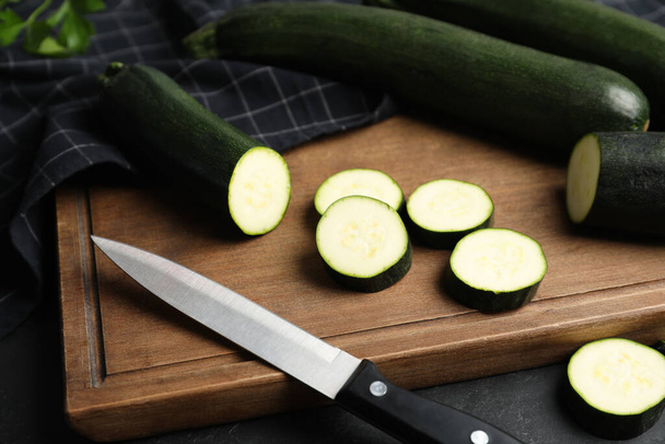 Green ripe zucchinis and wooden board on black slate table, closeup - Foto, afbeelding