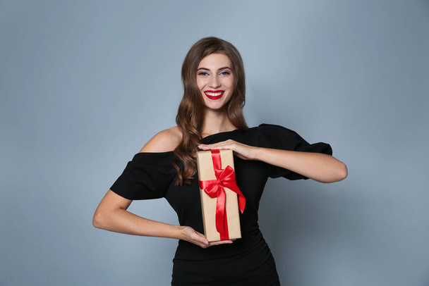 Happy woman with gift box on grey background. Christmas party - Valokuva, kuva