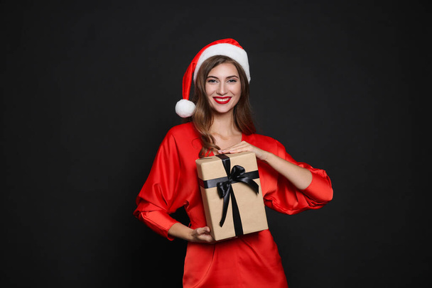 Happy woman in Santa hat with gift box on black background. Christmas party - Foto, Imagem