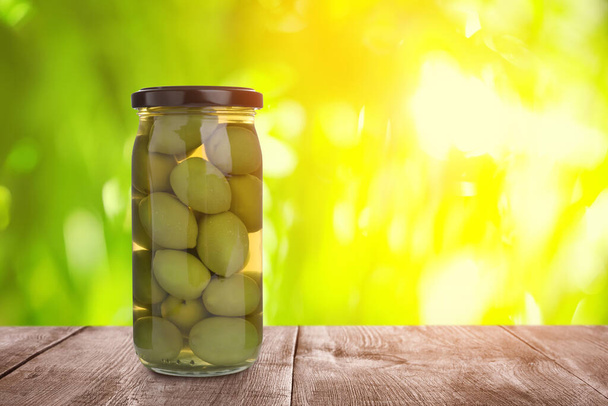 Jar of pickled olives on wooden table against blurred background, space for text - Foto, afbeelding