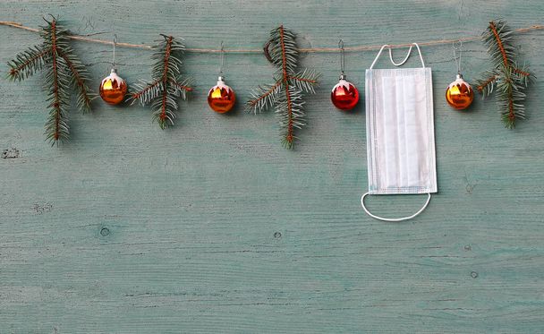 Corona and Christmas. A protective mask hangs next to Christmas tree balls and fir branches - Photo, Image